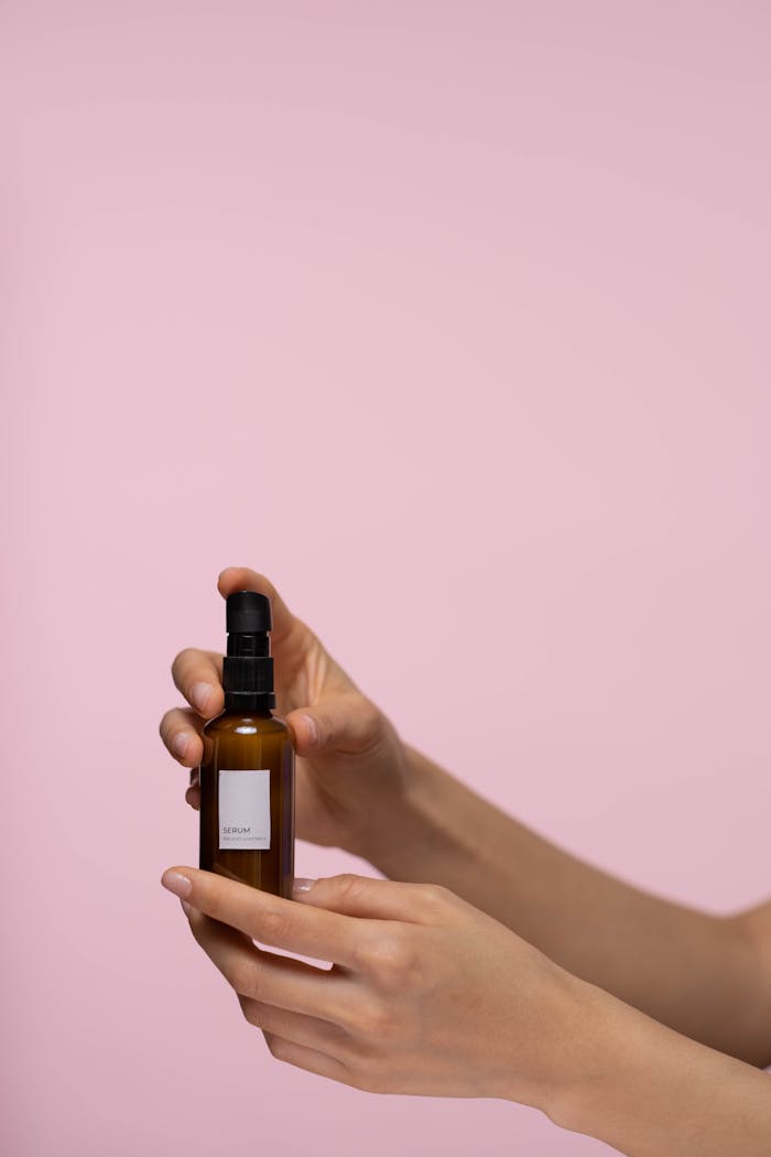 Hands holding a cosmetic spray bottle against a pink background, ideal for skincare promotions.