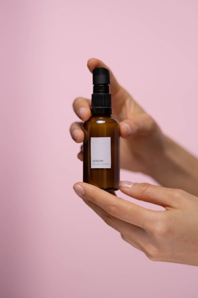 Close-up of hands holding a skincare serum bottle against a pink background, ideal for beauty promotion.